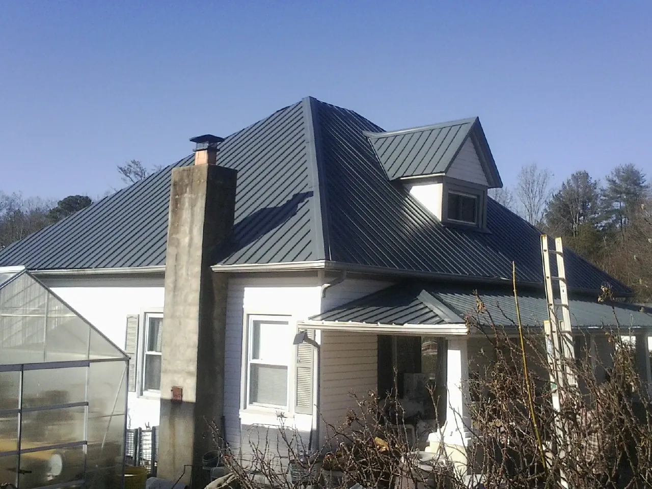 Dark blue standing seam metal roof on a white farmhouse with dormer — Slate & Tile Roof Repair by Roofing Brothers in Lostant
