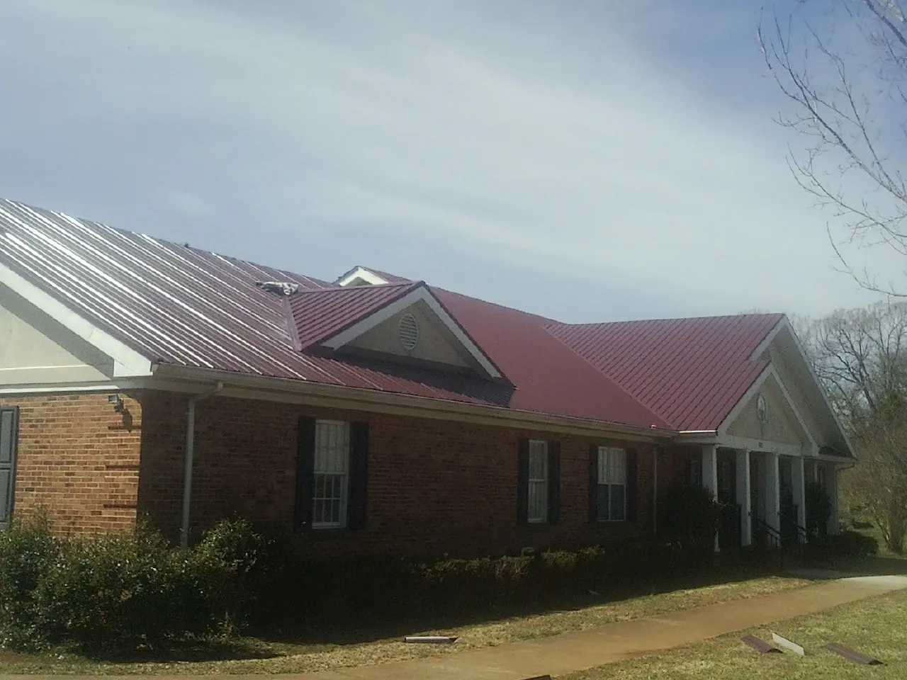 Red metal roof with gabled entries on a long brick building, from a Hail Damage Roof Repair job in Lostant