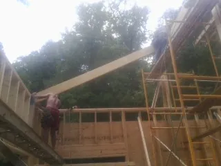 Carpenter raising a rafter beam on a new second story frame in Lostant