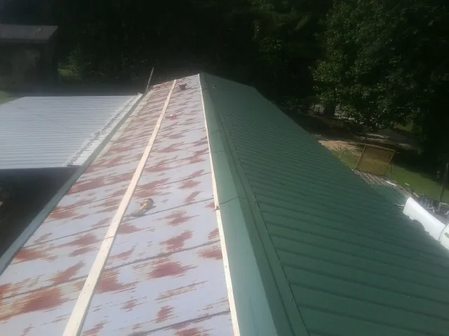 Old rusted panels beside newly installed green metal roofing — Wind Damage Roof Repair by Roofing Brothers in Lostant