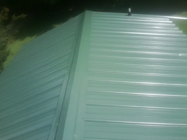 New green metal panels meeting at the ridge of a roof — Flat Roof Repair work by our crew in Lostant
