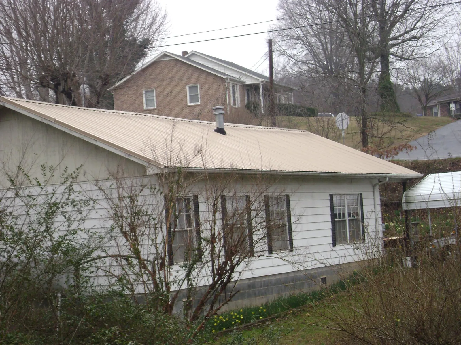 Tan metal roof on a white sided house set into a hillside — Commercial Roofing by Roofing Brothers in Lostant