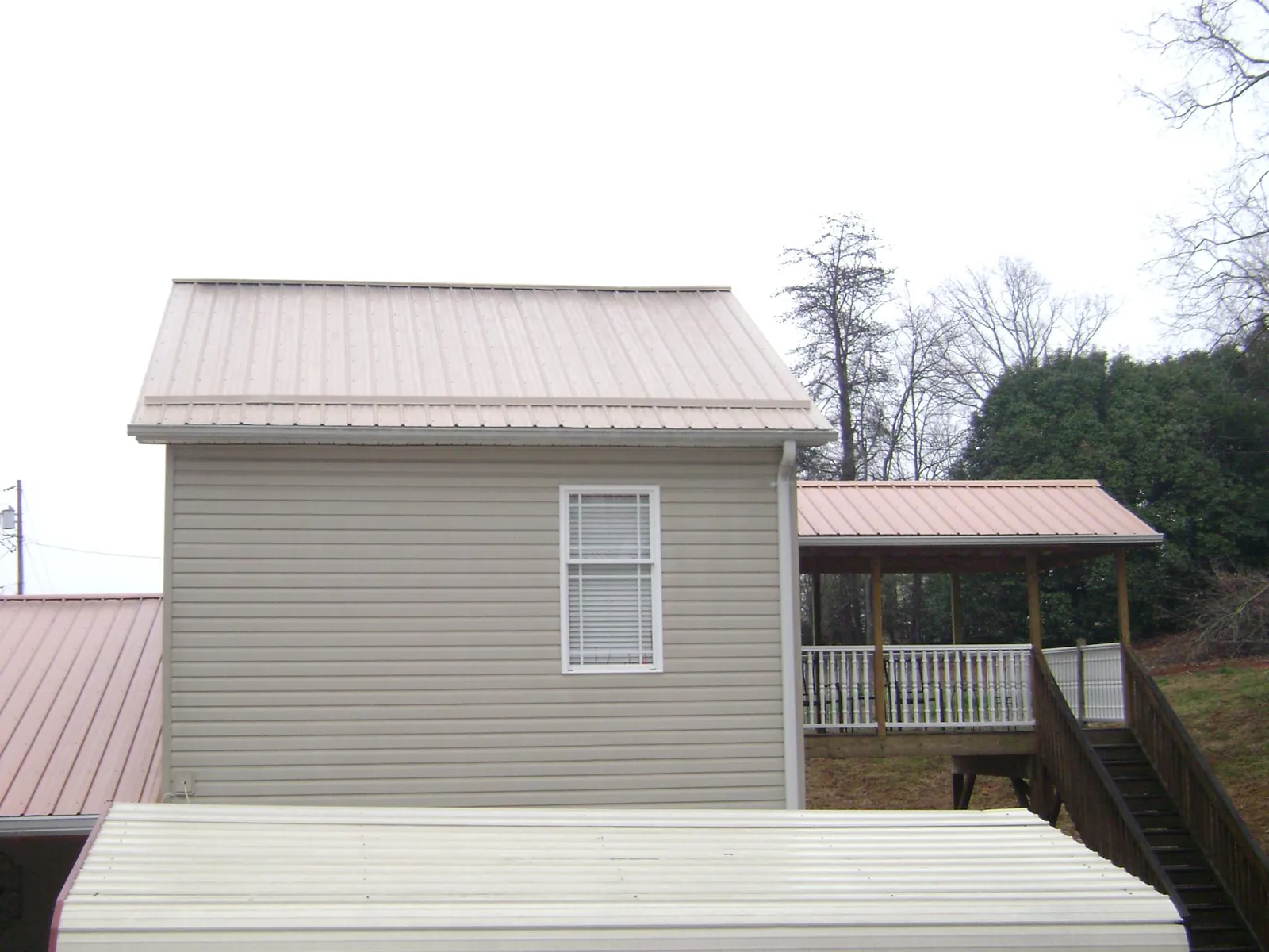 Tan metal roofs on a two story addition and attached porch, from a Roof Replacement job in Lostant